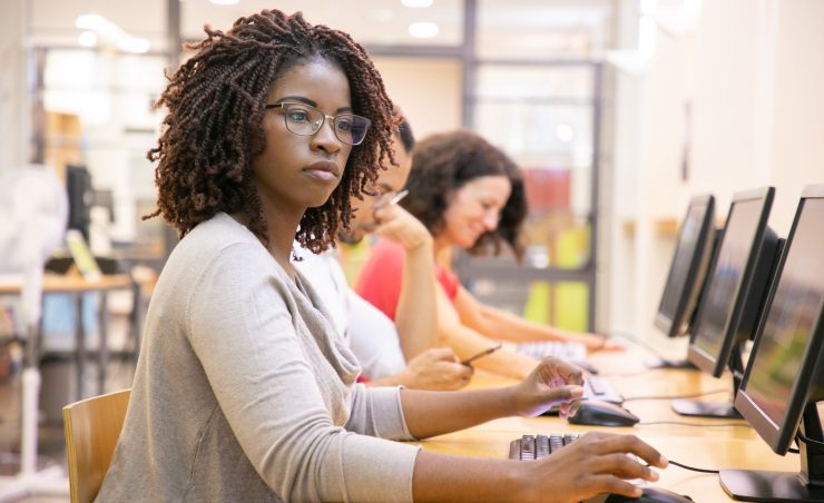 African American adult student working in computer class. Line of man and women in casual sitting at table, using desktops, typing. Staff training concept